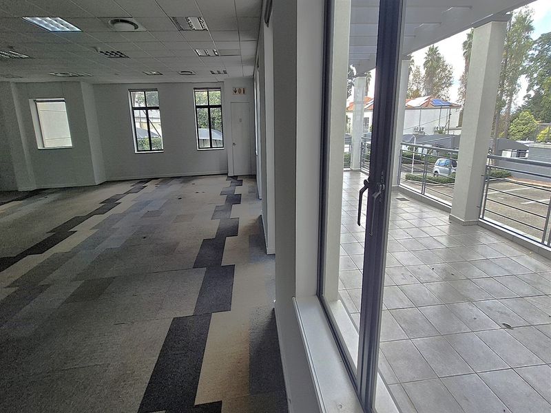Spacious empty office area featuring carpet tiles, recessed lighting, and direct access to a tiled balcony with metal railings.