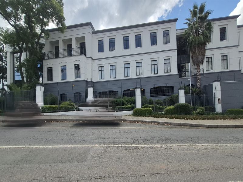 A professional multi-story office building facade featuring a modern exterior, secure perimeter fencing, and a well-maintained landscaped garden area.