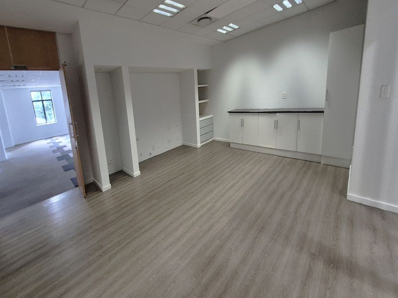 A bright, empty office space featuring modern laminate flooring, built-in storage cabinetry, and a suspended ceiling with recessed lighting.