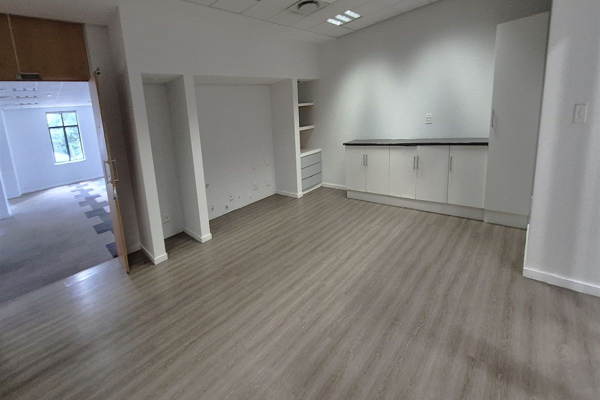 A bright, empty office space featuring modern laminate flooring, built-in storage cabinetry, and a suspended ceiling with recessed lighting.