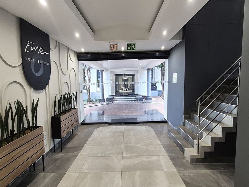 Modern office building entrance lobby featuring tiled flooring, decorative wall accents, and a staircase with stainless steel railings leading to the main glass doors.