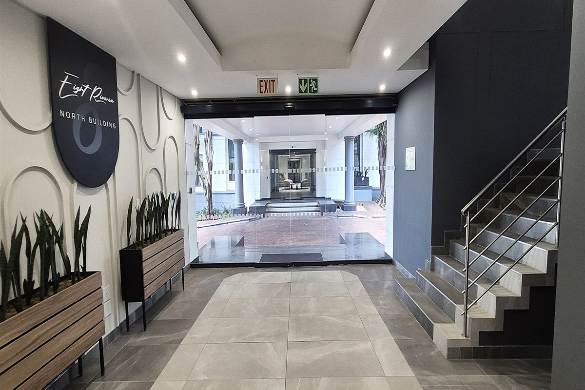 Modern office building entrance lobby featuring tiled flooring, decorative wall accents, and a staircase with stainless steel railings leading to the main glass doors.