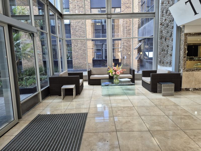 Bright and modern office building entrance lobby featuring floor-to-ceiling glass walls, polished stone flooring, and a decorative textured stone feature wall.