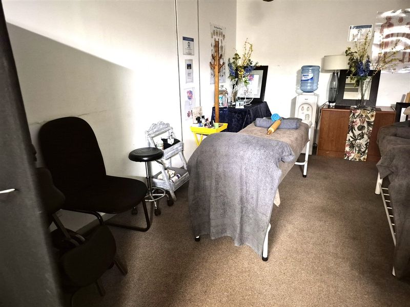 A functional office space currently utilized as a treatment room, featuring carpeted flooring and neutral wall finishes.