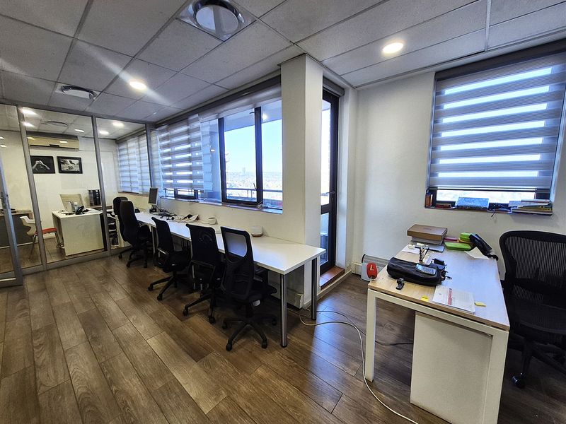 A modern office space featuring laminate flooring, a suspended ceiling with recessed lighting, and large windows with roller blinds providing natural light.