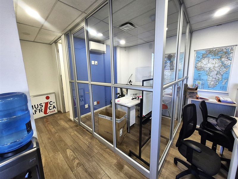 A modern office space featuring a glass-partitioned private office, suspended ceiling with recessed lighting, and durable wood-look flooring.