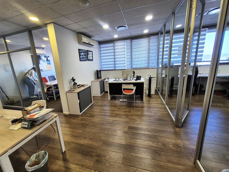 Modern office space featuring glass partition walls, wood-look flooring, suspended ceilings with recessed lighting, and integrated air conditioning.