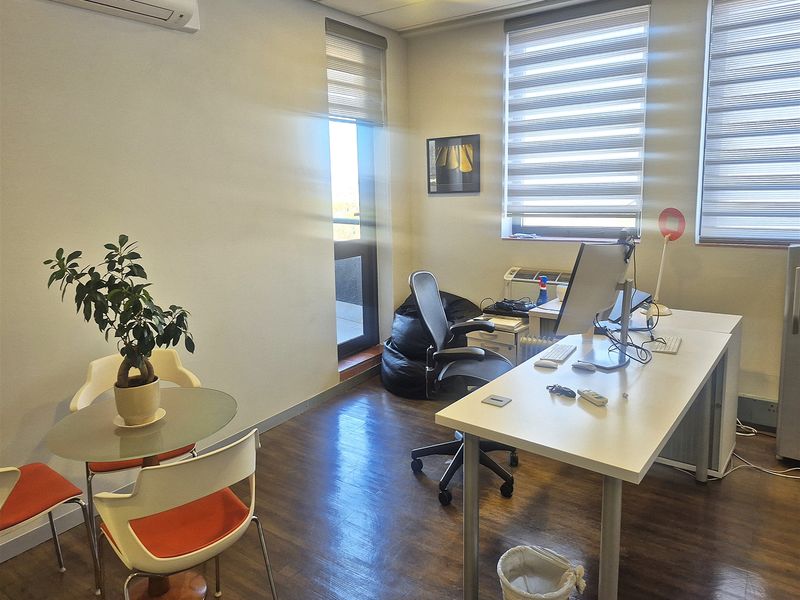 A functional office space featuring laminate flooring, split-system air conditioning, and large windows with roller blinds for natural light.