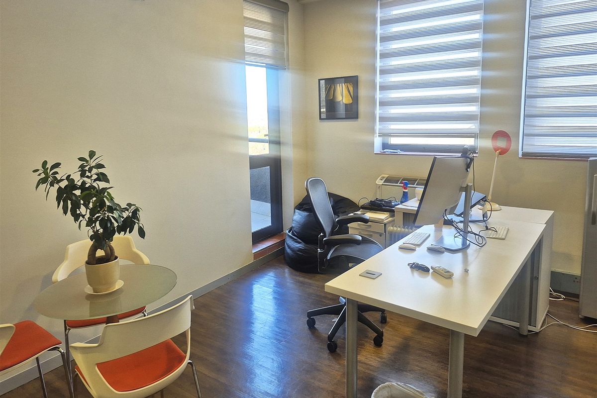 A functional office space featuring laminate flooring, split-system air conditioning, and large windows with roller blinds for natural light.