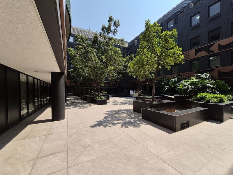 A well-maintained modern office courtyard featuring tiled flooring, built-in planters with mature trees, and a contemporary dark-toned building facade.