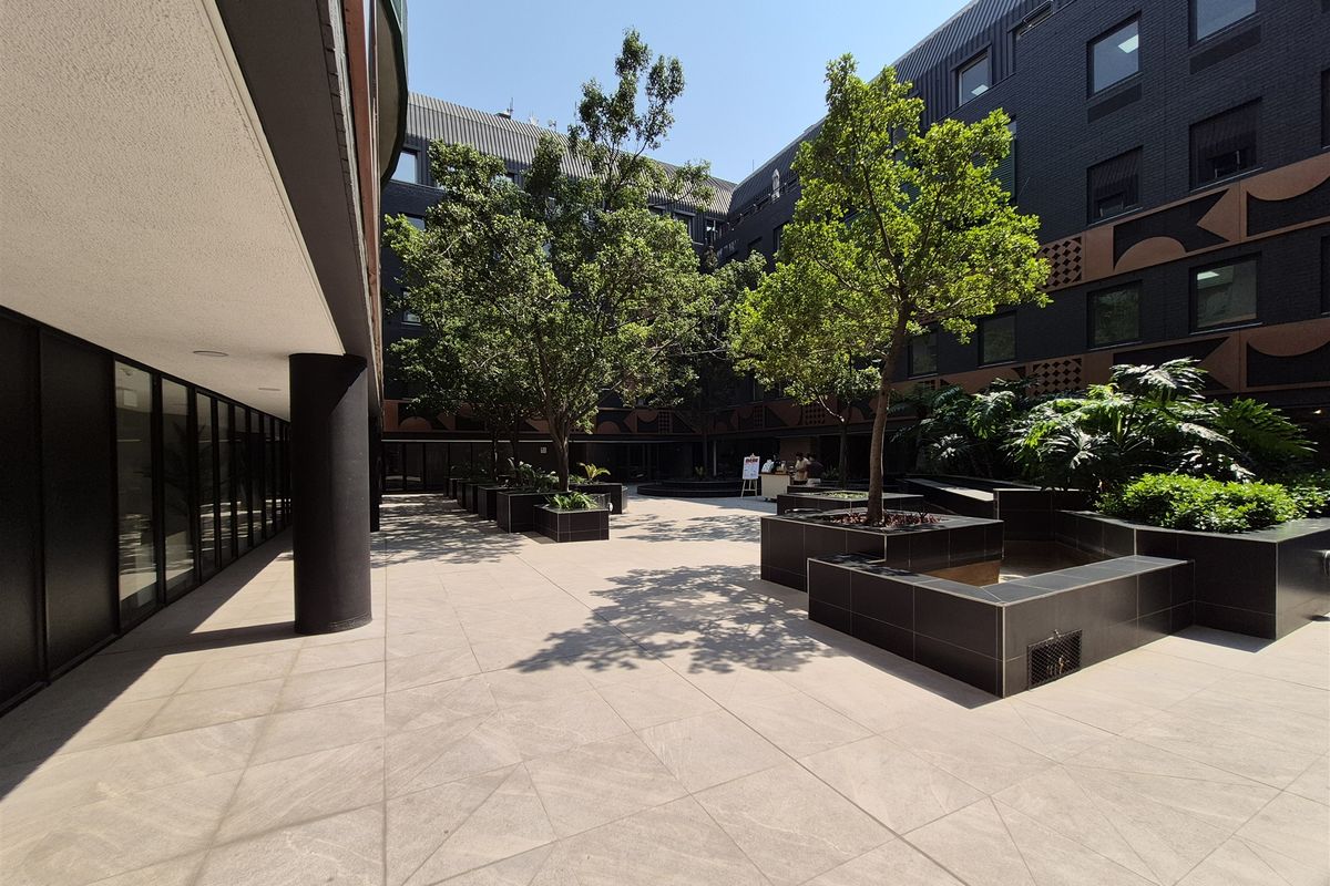 A well-maintained modern office courtyard featuring tiled flooring, built-in planters with mature trees, and a contemporary dark-toned building facade.