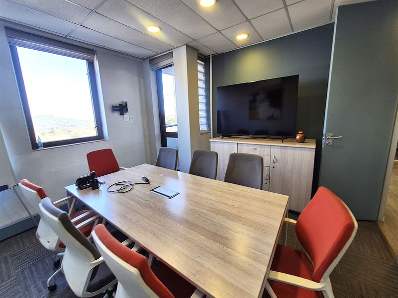 A functional office meeting room featuring a large window, suspended ceiling with recessed lighting, and built-in storage cabinetry.