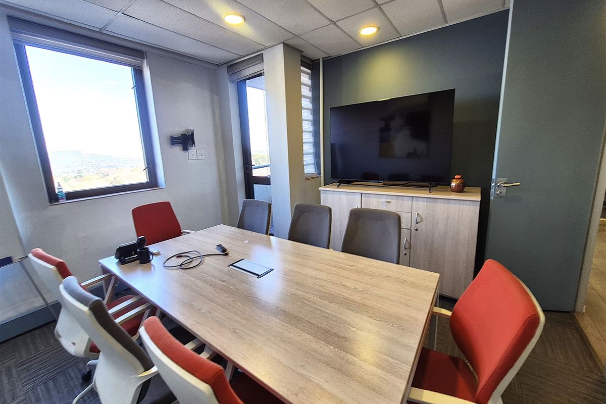 A functional office meeting room featuring a large window, suspended ceiling with recessed lighting, and built-in storage cabinetry.
