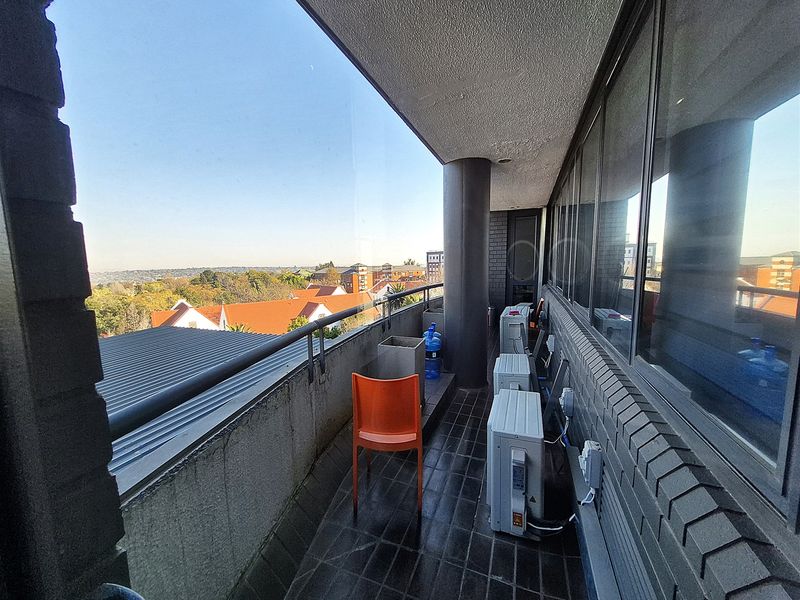 A spacious balcony featuring tiled flooring, metal railings, and large glass windows, offering an elevated view of the surrounding area.