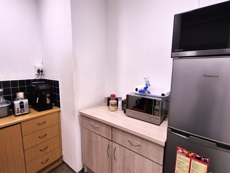 A compact office kitchenette featuring laminate cabinetry, a black tiled backsplash, and integrated microwave space, providing functional utility for staff.