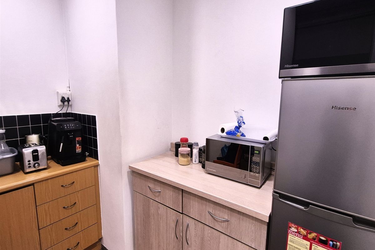 A compact office kitchenette featuring laminate cabinetry, a black tiled backsplash, and integrated microwave space, providing functional utility for staff.