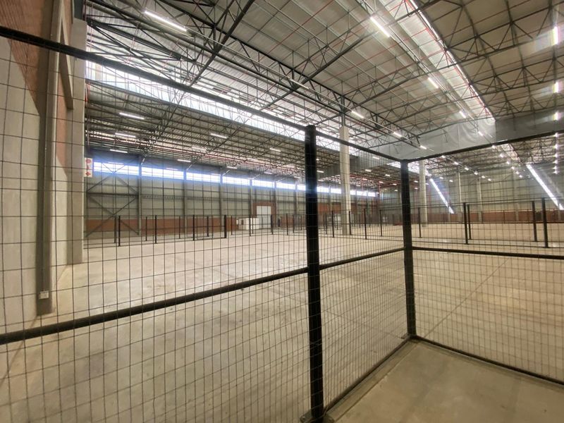 Spacious industrial warehouse interior featuring high steel truss ceilings, concrete flooring, and secure wire mesh partitioning throughout the open floor plan.