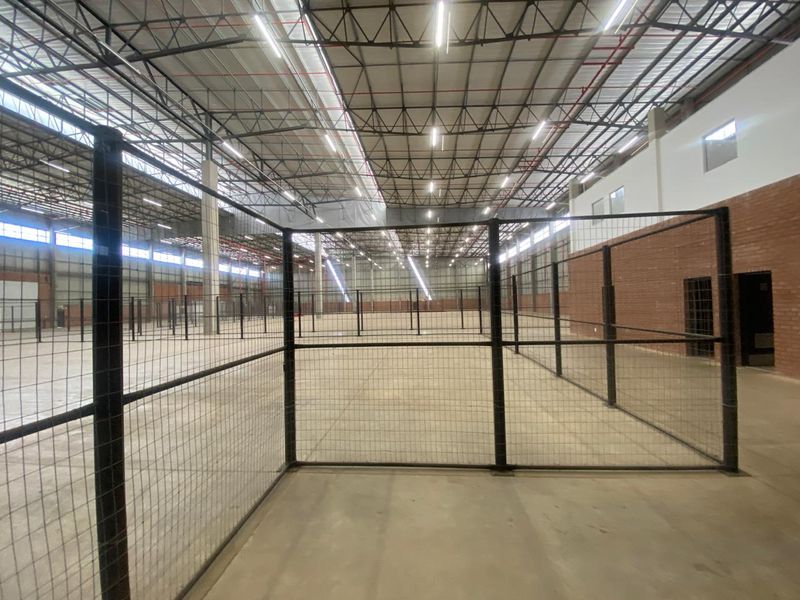 Spacious industrial warehouse interior featuring high exposed steel roof trusses, concrete flooring, and secure wire mesh partitioning throughout the open floor plan.