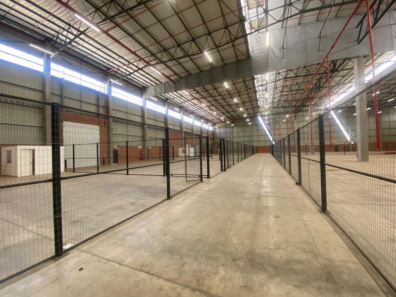 Large industrial warehouse space featuring high ceilings, concrete flooring, fire sprinkler systems, and wire mesh partitioning for organized storage or operational zones.