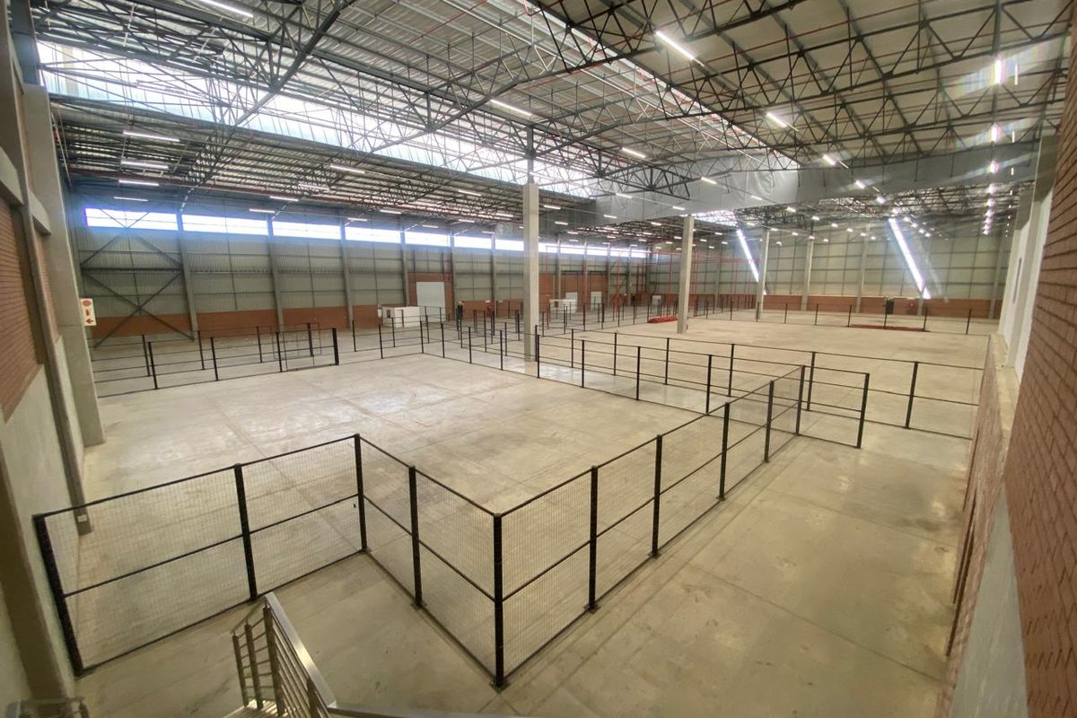 Expansive industrial warehouse space featuring high ceilings with exposed steel trusses, concrete flooring, and modular metal mesh partitioning throughout the open floor plan.