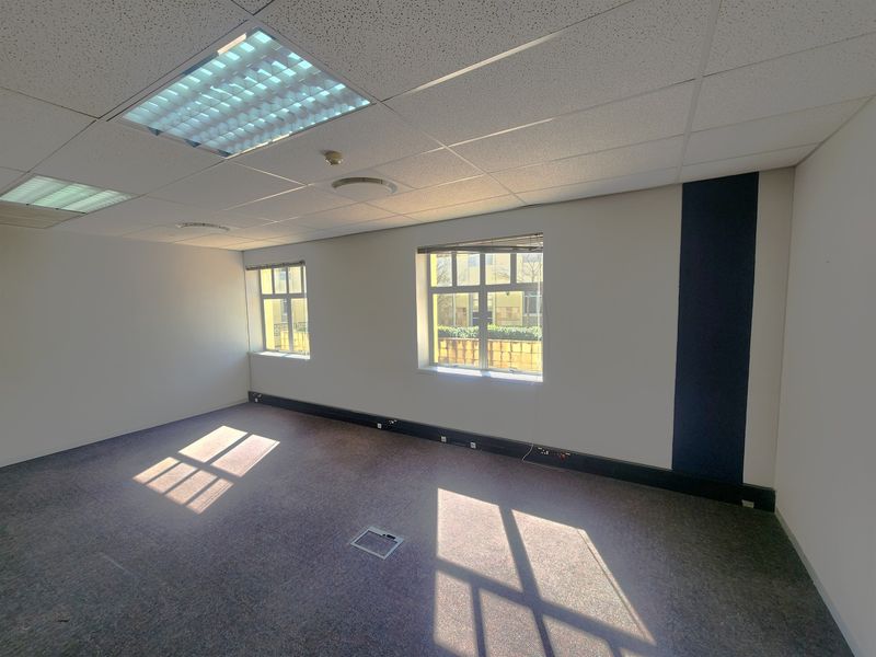A vacant, well-lit office space featuring a suspended ceiling, recessed lighting, carpeted flooring, and integrated floor power outlets.