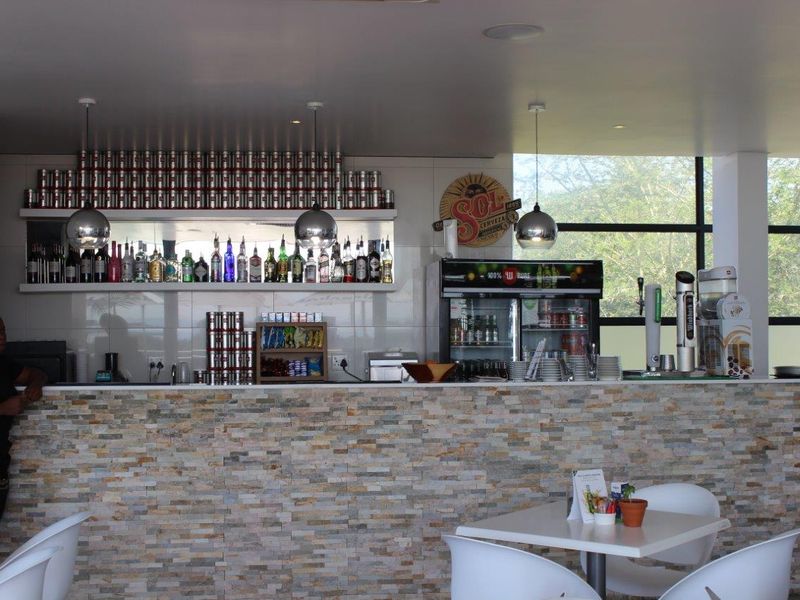 A well-maintained bar area featuring a stone-clad counter, built-in shelving for display, and modern pendant lighting with large windows providing natural light.