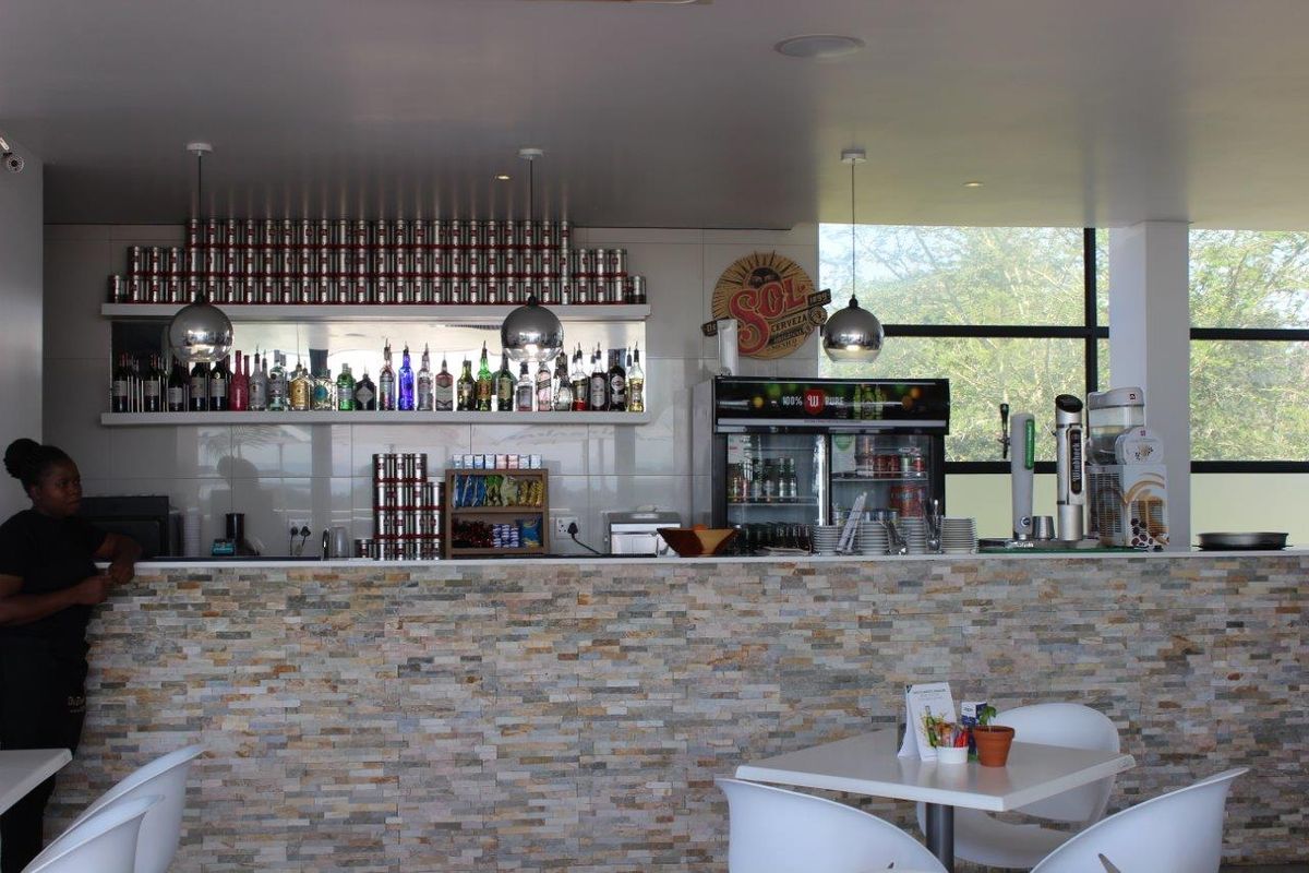 A well-maintained bar area featuring a stone-clad counter, built-in shelving for display, and modern pendant lighting with large windows providing natural light.