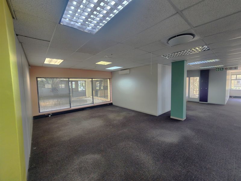 An empty, open-plan office space featuring a suspended ceiling, recessed lighting, air conditioning, and large windows overlooking an exterior courtyard.