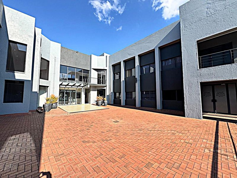 A spacious paved courtyard area situated between modern office building wings, featuring large glass windows and a clean, functional architectural design.