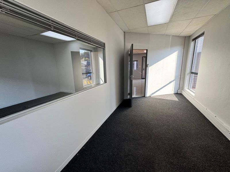A vacant office space featuring carpeted flooring, a suspended ceiling with recessed lighting, and an internal glass partition wall.