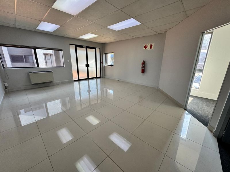 A bright, vacant office space featuring polished ceramic floor tiles, a suspended ceiling with recessed lighting, and an integrated air conditioning unit.