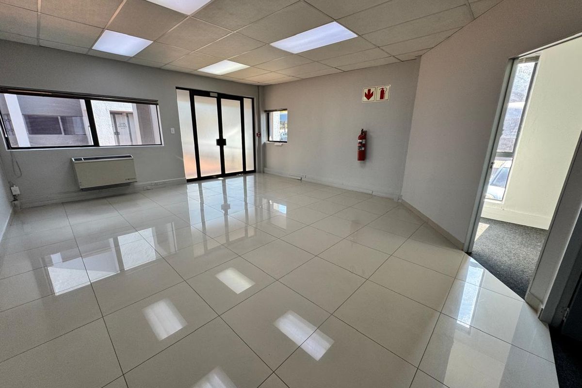 A bright, vacant office space featuring polished ceramic floor tiles, a suspended ceiling with recessed lighting, and an integrated air conditioning unit.
