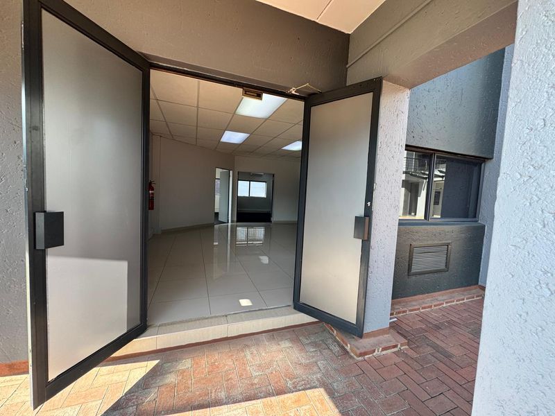 Entrance to an office space featuring double glass doors, tiled flooring, and a suspended ceiling with recessed lighting, opening onto a brick-paved patio area.