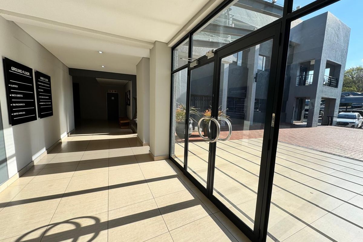 Modern office building entrance lobby featuring large glass doors, tiled flooring, and clear directory signage for ground and first floor tenants.