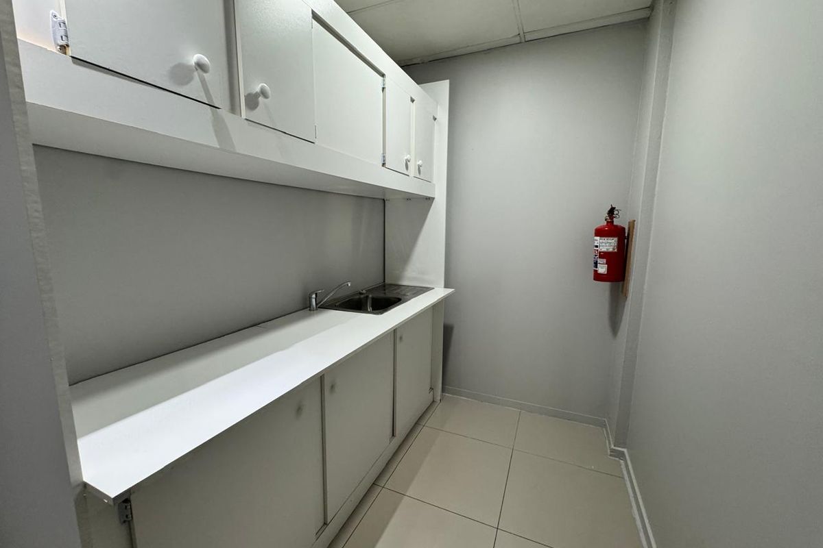 A functional office kitchenette featuring built-in white cabinetry, a stainless steel sink, tiled flooring, and a wall-mounted fire extinguisher.