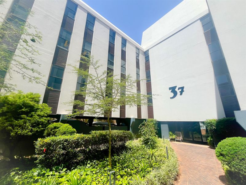 Front exterior view of a multi-story office building featuring a paved entrance walkway and well-maintained landscaped garden.