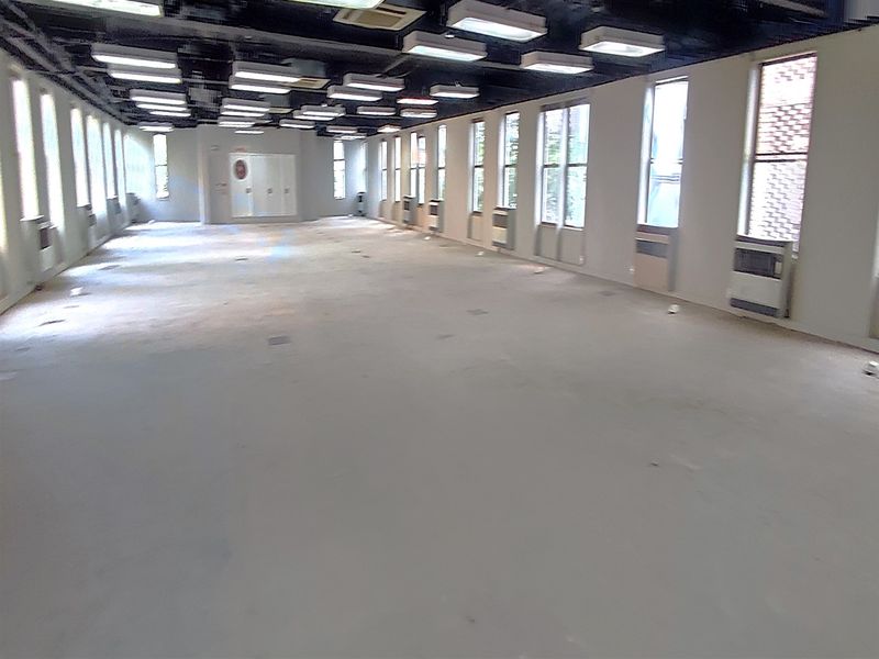 A large, vacant open-plan office space featuring exposed ceilings, multiple windows, and integrated HVAC units, ready for custom fit-out.
