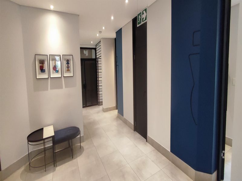 A clean, modern office hallway featuring neutral tiled flooring, recessed downlighting, and contemporary blue and white wall accents.