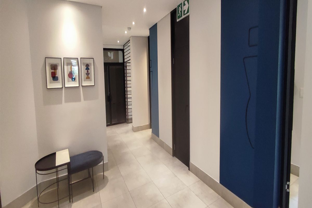A clean, modern office hallway featuring neutral tiled flooring, recessed downlighting, and contemporary blue and white wall accents.