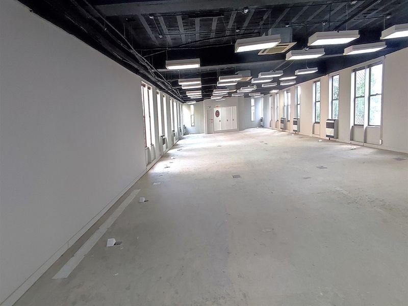 A spacious, open-plan office area featuring an exposed ceiling, large windows for natural light, and practical floor power outlets throughout the workspace.