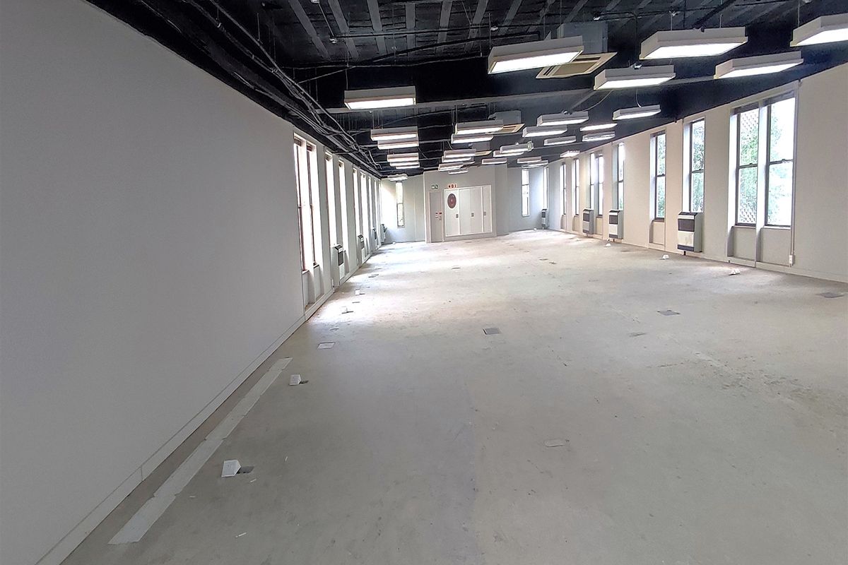 A spacious, open-plan office area featuring an exposed ceiling, large windows for natural light, and practical floor power outlets throughout the workspace.