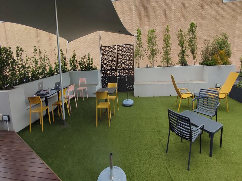 Outdoor rooftop patio area featuring artificial turf, a shade sail, built-in concrete bench seating, and decorative privacy screening.