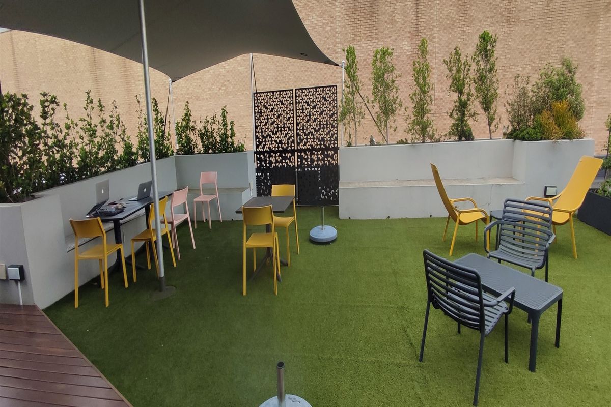 Outdoor rooftop patio area featuring artificial turf, a shade sail, built-in concrete bench seating, and decorative privacy screening.