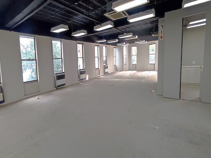Spacious open-plan office area featuring an exposed ceiling, multiple windows for natural light, and integrated air conditioning units.