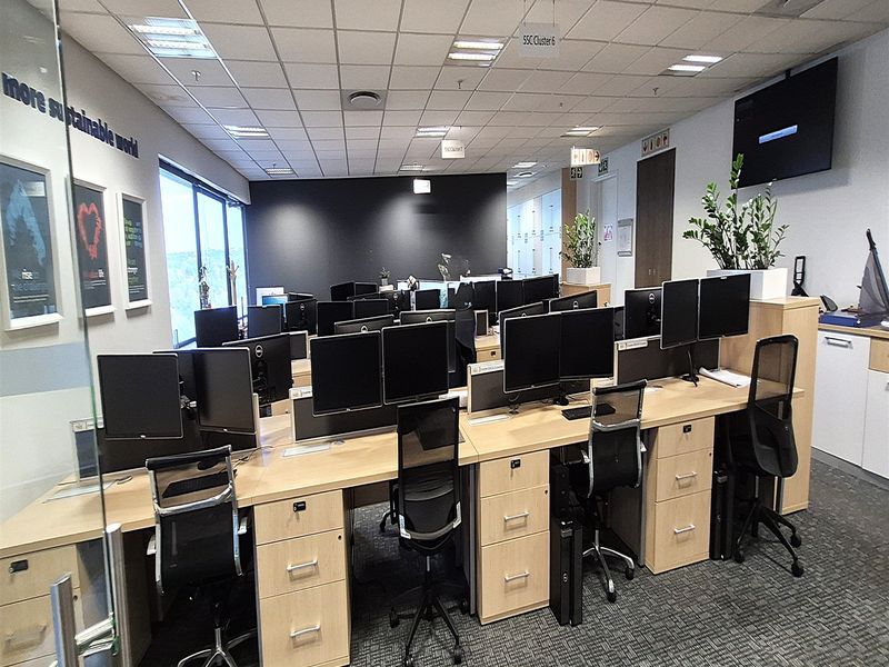 A professional open-plan office space featuring multiple built-in workstations, suspended ceilings with recessed lighting, and modern carpeted flooring.