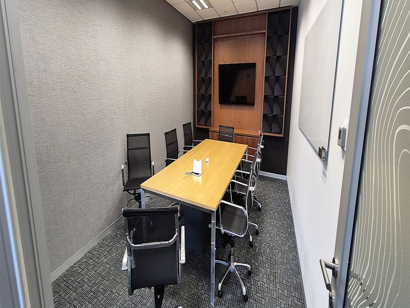 A professional meeting room featuring acoustic wall treatments, a built-in media console, integrated lighting, and a wall-mounted whiteboard.