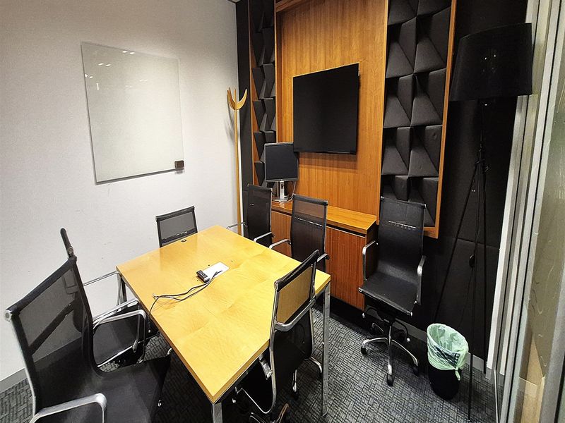 A professional meeting room featuring acoustic wall paneling, built-in cabinetry, a glass whiteboard, and a suspended ceiling.