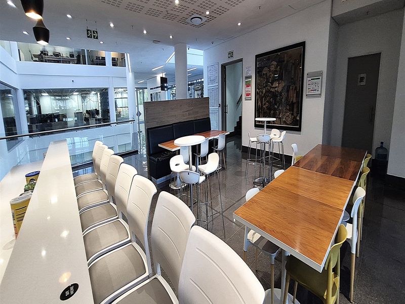 Modern open-plan office breakout area featuring polished tile flooring, acoustic ceiling panels, and a built-in breakfast bar overlooking the lower level.