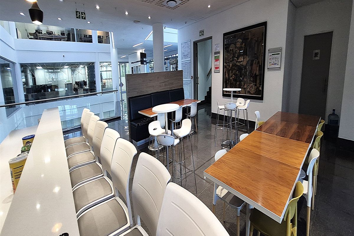 Modern open-plan office breakout area featuring polished tile flooring, acoustic ceiling panels, and a built-in breakfast bar overlooking the lower level.