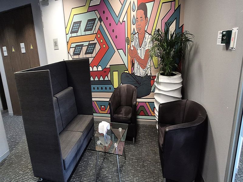 A modern office breakout area featuring a vibrant wall mural, carpeted flooring, and professional seating arrangements.